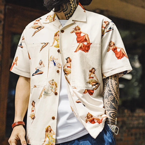 Person wearing a white shirt with vintage-style pin-up girl print, with tattoos visible on arms.